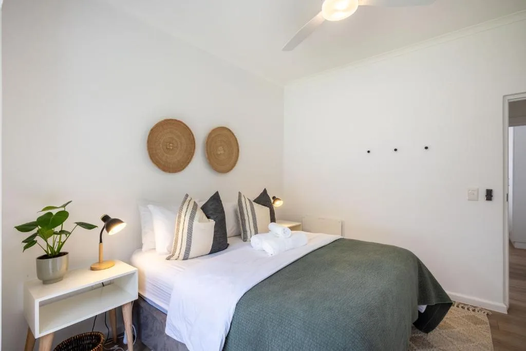 Modern bedroom with white bedding, decorative pillows, and woven wall art