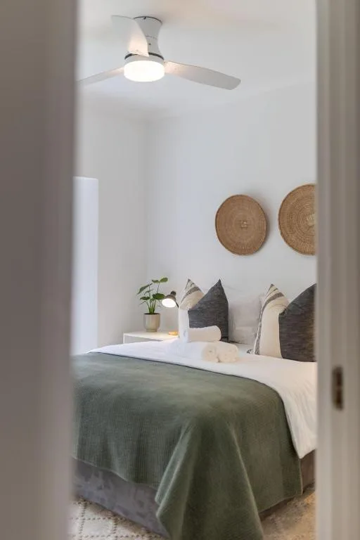 Serene bedroom with green bedding, woven wall decor, and ceiling fan