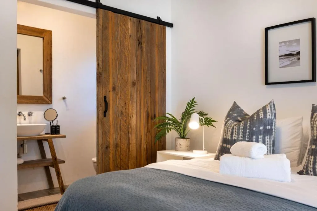 Modern bedroom with white bedding, wooden barn door, and ensuite bathroom access