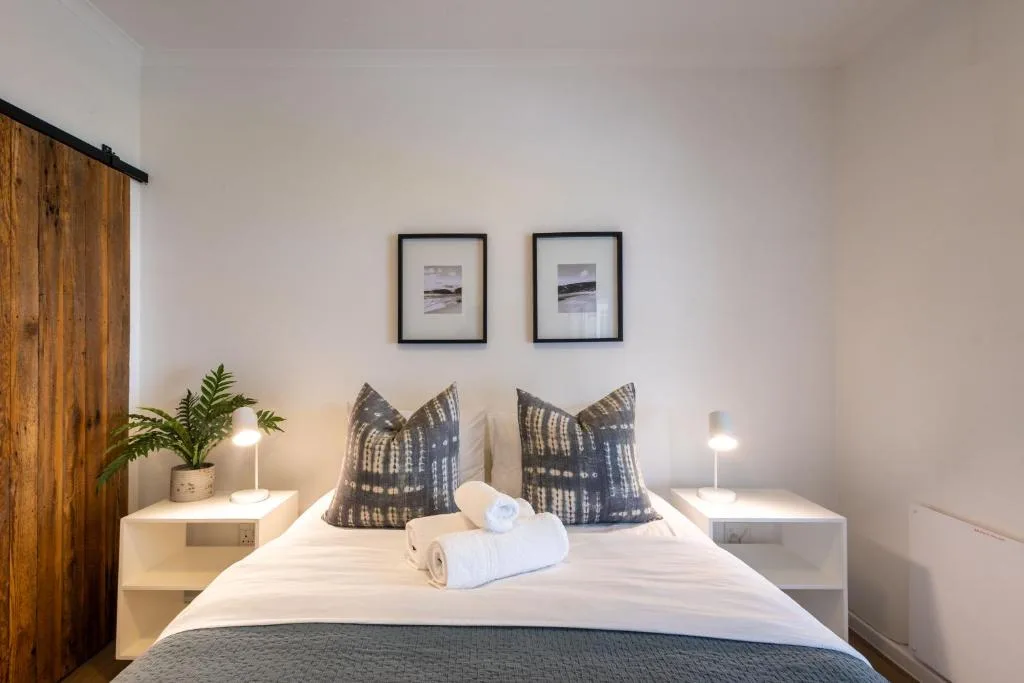 Modern bedroom with white bedding, patterned pillows, and framed coastal artwork