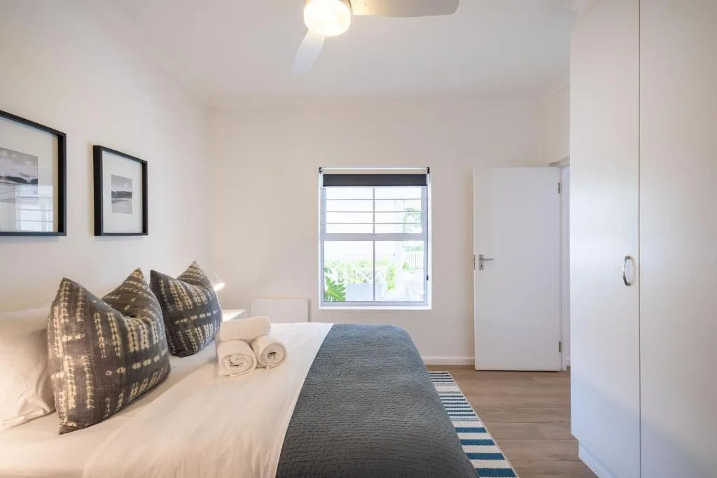 Bright bedroom with white bedding, patterned pillows, and rolled towels