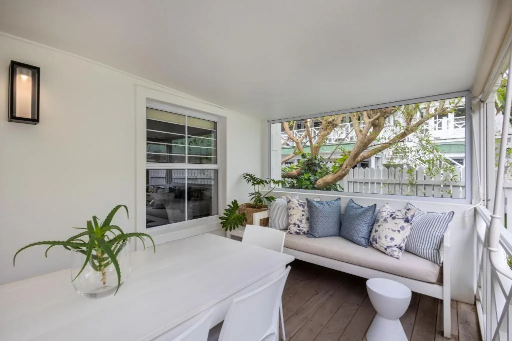Covered deck with white bench seating, cushions, and garden views
