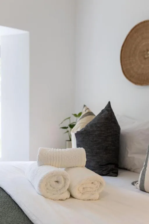 Rolled towels and cushions arranged on bed with woven wall decoration