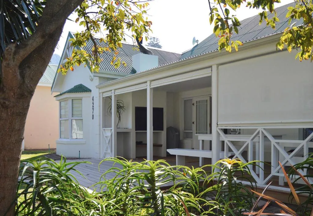 White cottage with green roof and covered porch, Garden Route garden setting