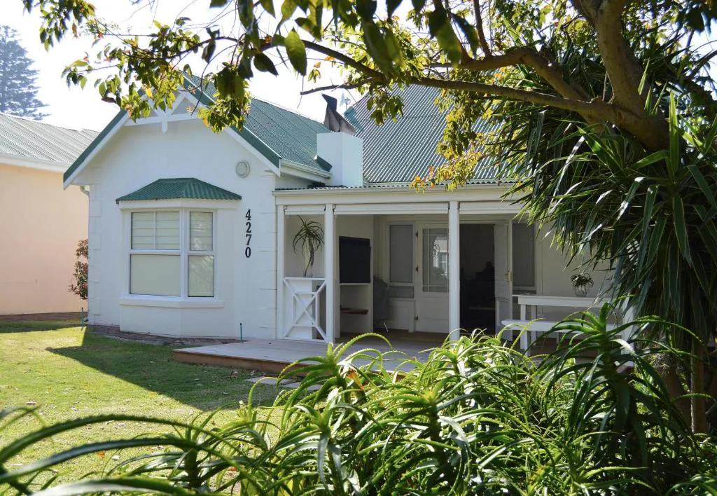White cottage with green roof and wide entrance deck, landscaped garden