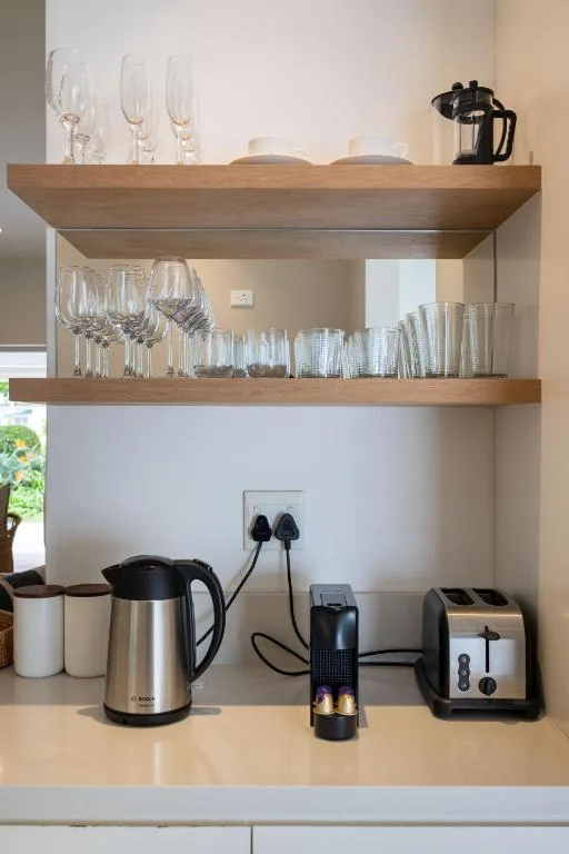 Kitchen counter with shelving displaying glasses, mugs, kettle, and coffee maker