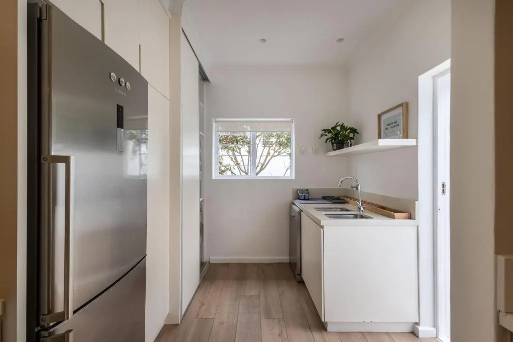 Modern kitchen with stainless steel refrigerator, white cabinetry, and window