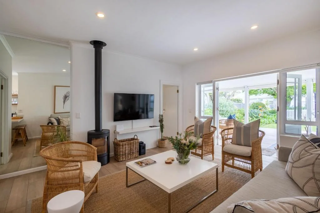 Bright open-plan lounge with woven chairs, fireplace, and garden views