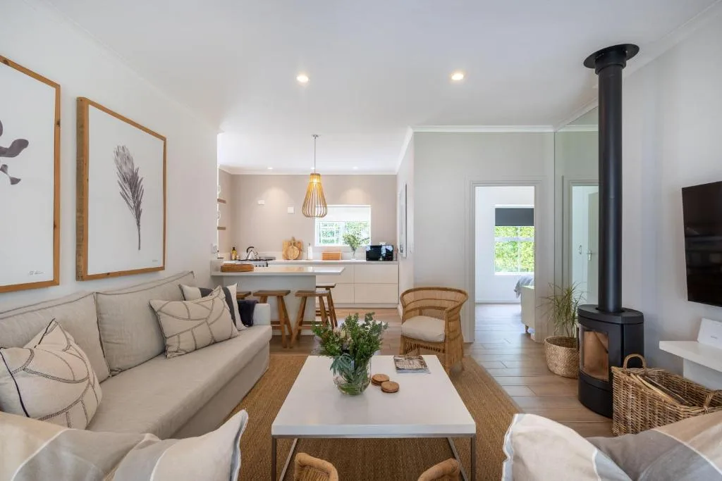 Modern open-plan lounge with cream sofa, wood stove, and kitchen visible beyond