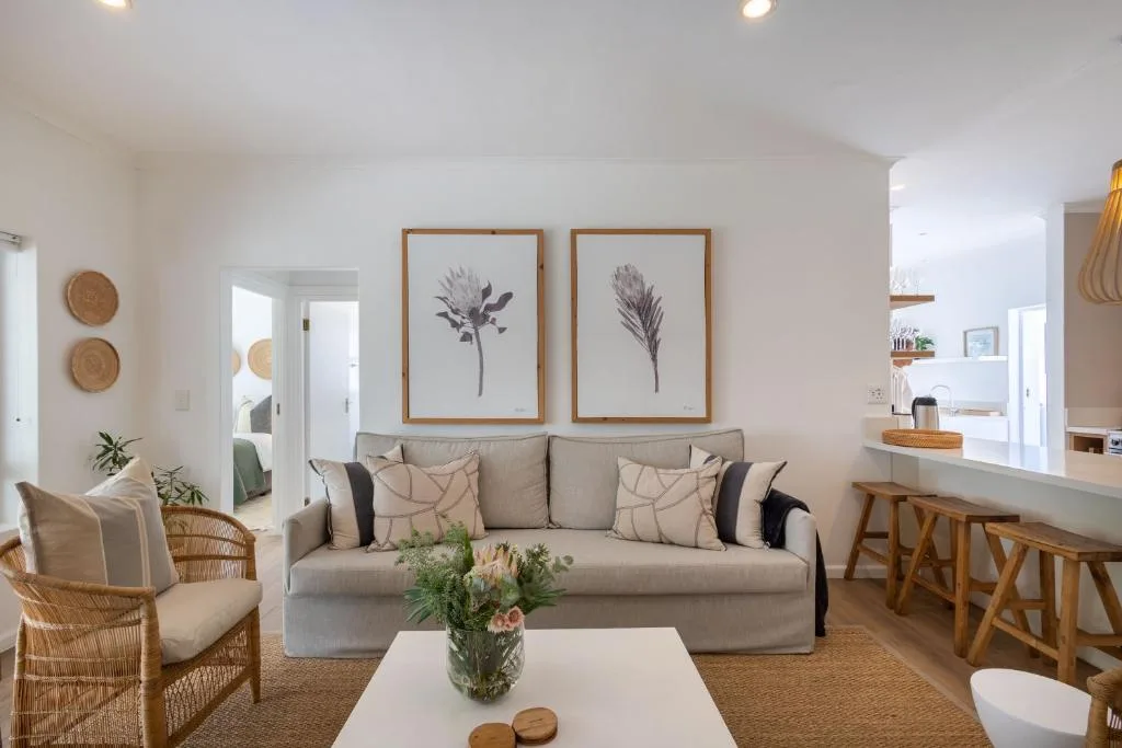 Bright open-plan lounge with beige sofa, rattan armchairs, botanical artwork
