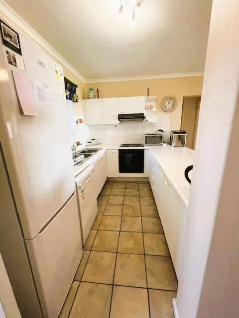 Compact galley kitchen with white cabinetry, refrigerator, and stovetop
