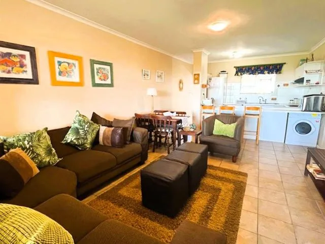 Open-plan lounge with brown sofa, colorful cushions, and kitchen visible