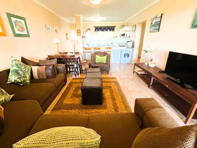 Open-plan lounge with brown sofas, TV, and kitchen visible in background