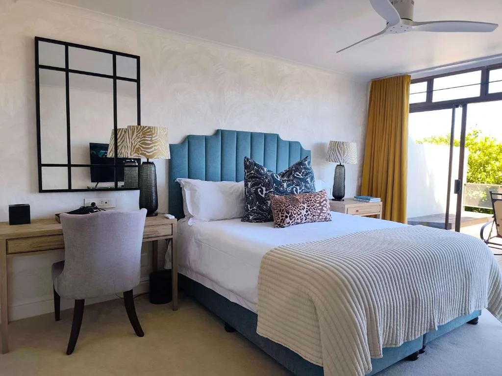 Spacious bedroom with blue upholstered bed and ocean view through glass doors