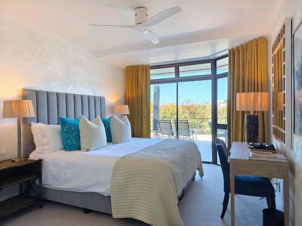 Modern bedroom with king bed, coastal view through glass doors to deck
