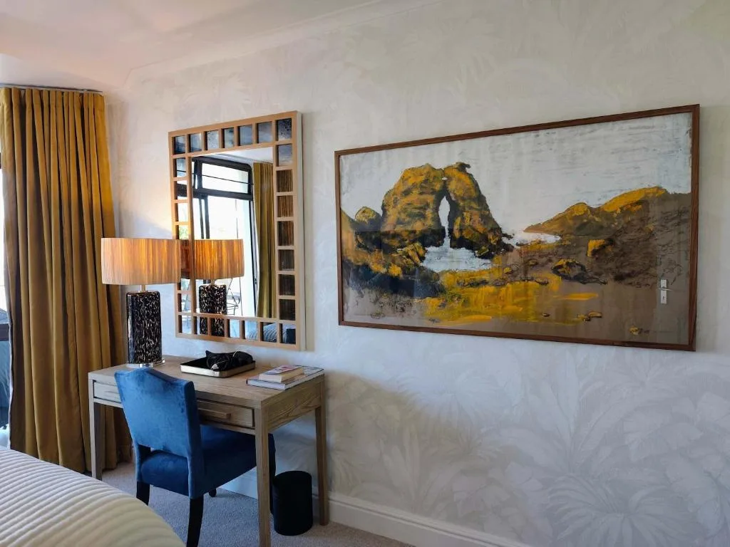 Bedroom workspace with desk, mirror, lamp, and coastal rock artwork