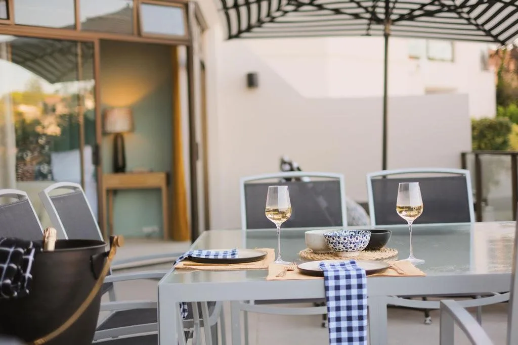 Outdoor dining table with wine glasses and place settings under pergola