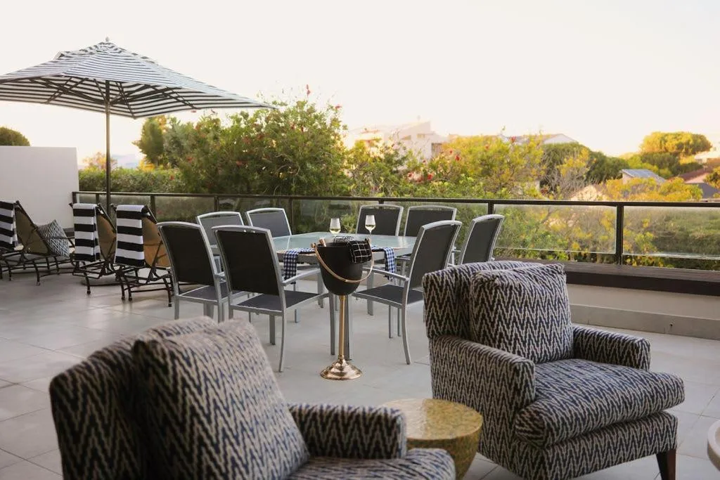 Spacious outdoor terrace with lounge seating and striped umbrella overlooking lush gardens