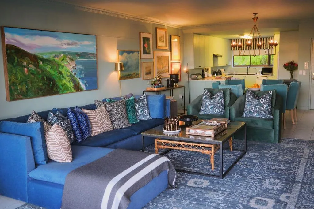 Spacious living room with blue sofa, green armchairs, and coastal landscape artwork