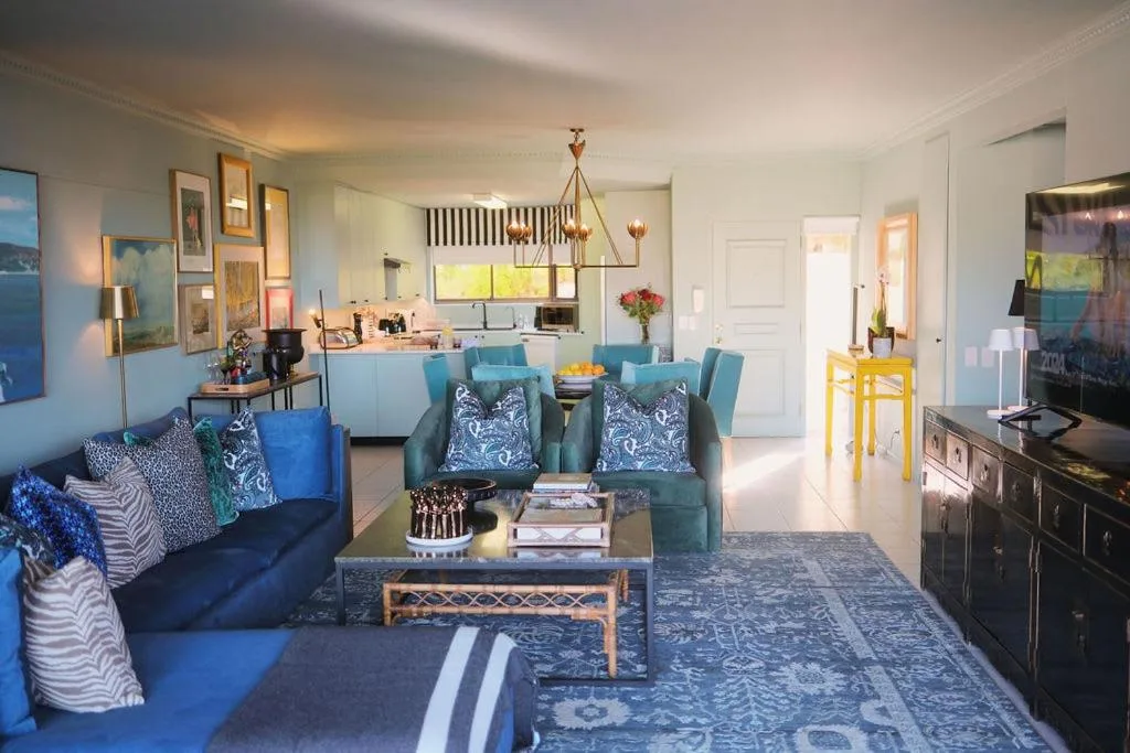 Bright open-plan lounge with blue sofas, patterned cushions, and flat-screen TV