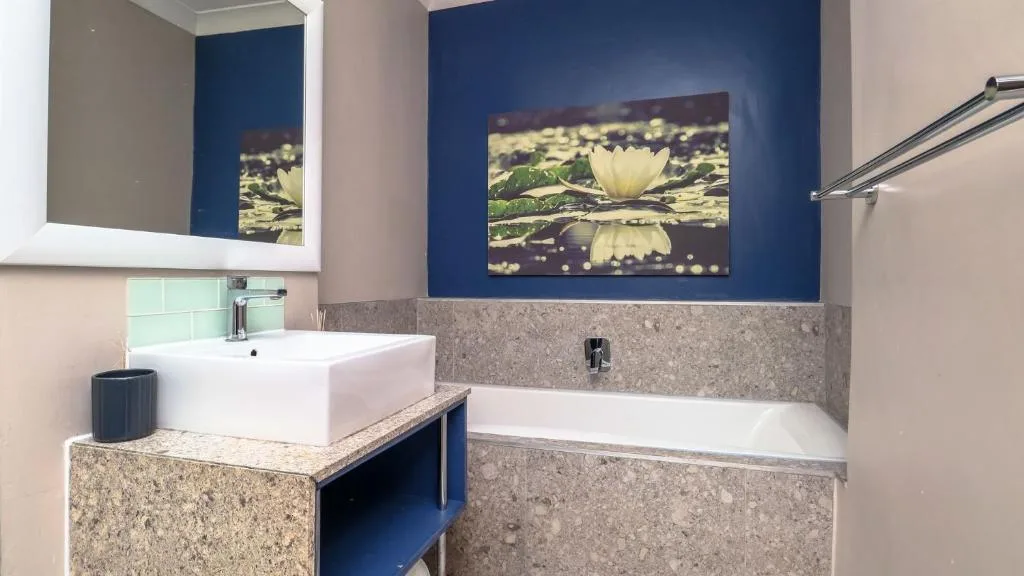 Modern bathroom with white basin, bathtub, and blue accent wall artwork
