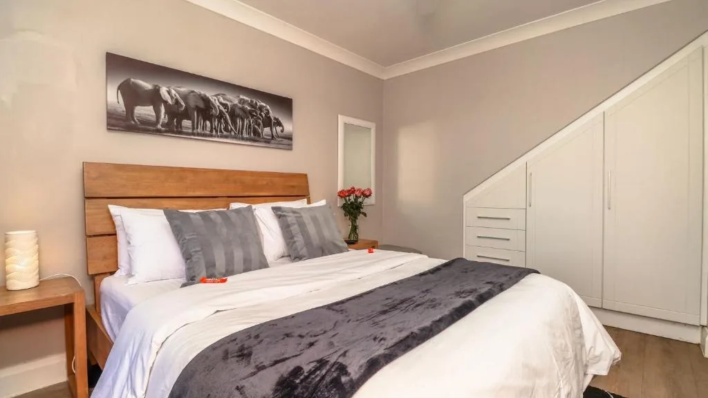 Spacious bedroom with wooden bed frame, crisp linens, fresh flowers, and built-in wardrobe.