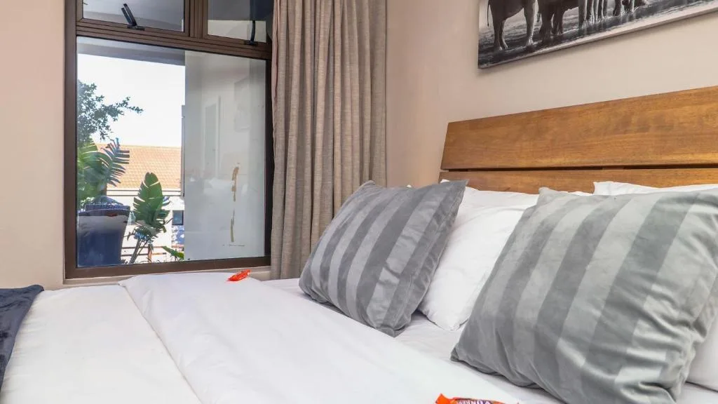 Bedroom with wooden headboard, striped pillows, white bedding, and garden view