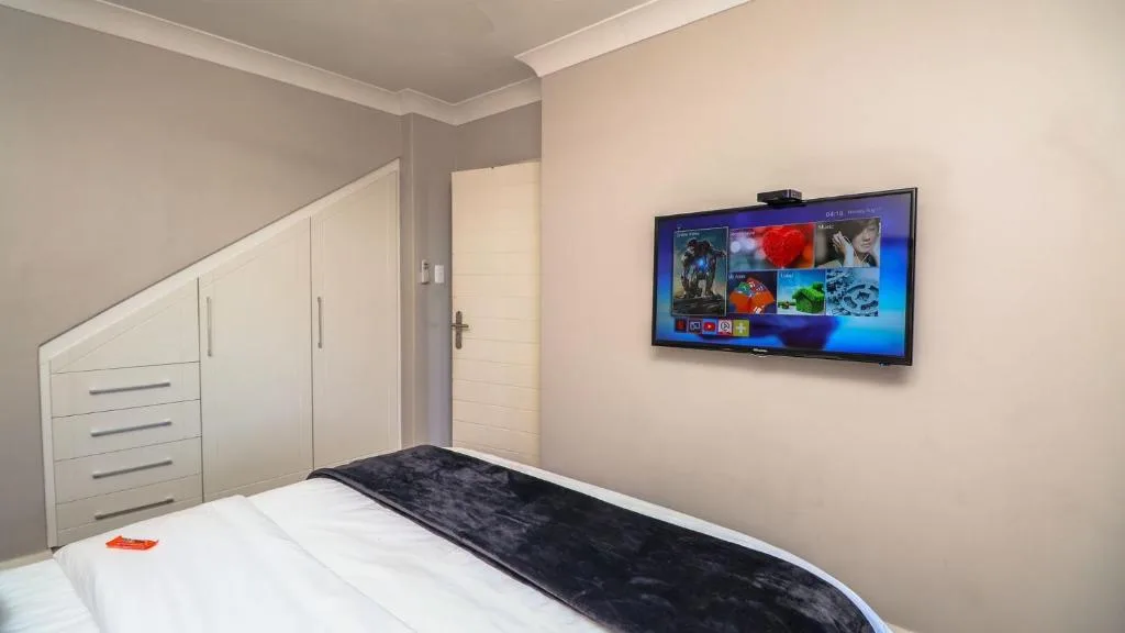 Modern bedroom with white bedding, wall-mounted TV, and built-in wardrobe