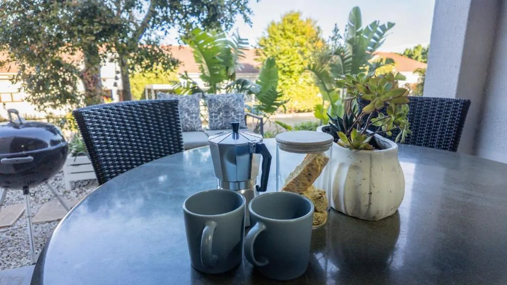 Outdoor patio table with coffee service and potted plants, garden view