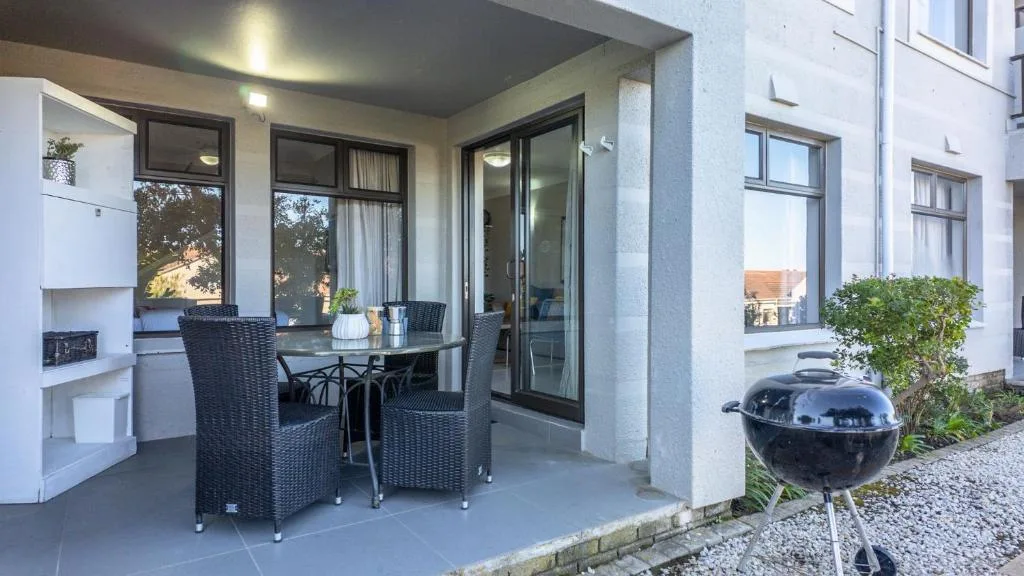 Covered patio with dining table, wicker chairs, and braai grill