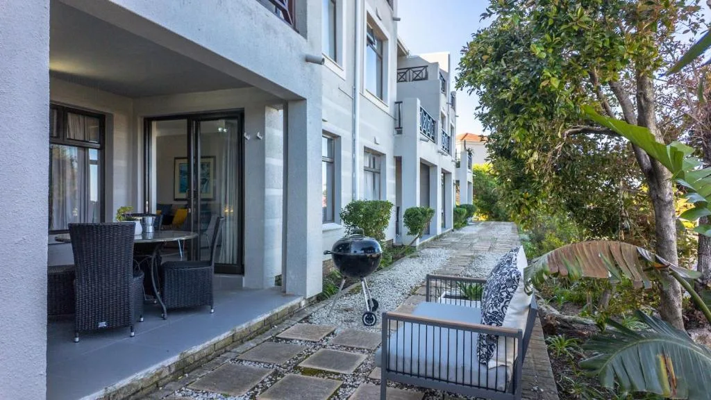 Modern white apartment building with patio seating and manicured garden pathway
