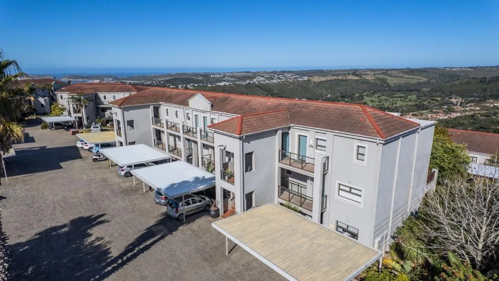 Modern white apartment building with terracotta roof and parking area overlooking valley