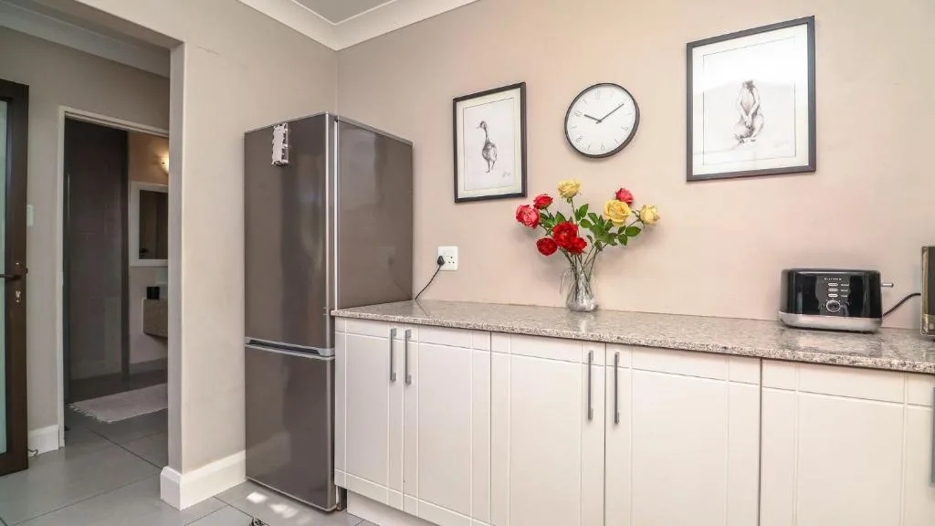 Modern kitchen with stainless steel fridge, white cabinetry, granite countertop, fresh flowers