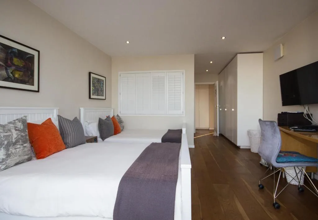Spacious bedroom with white bed, colorful pillows, and flat-screen TV mounted on wall