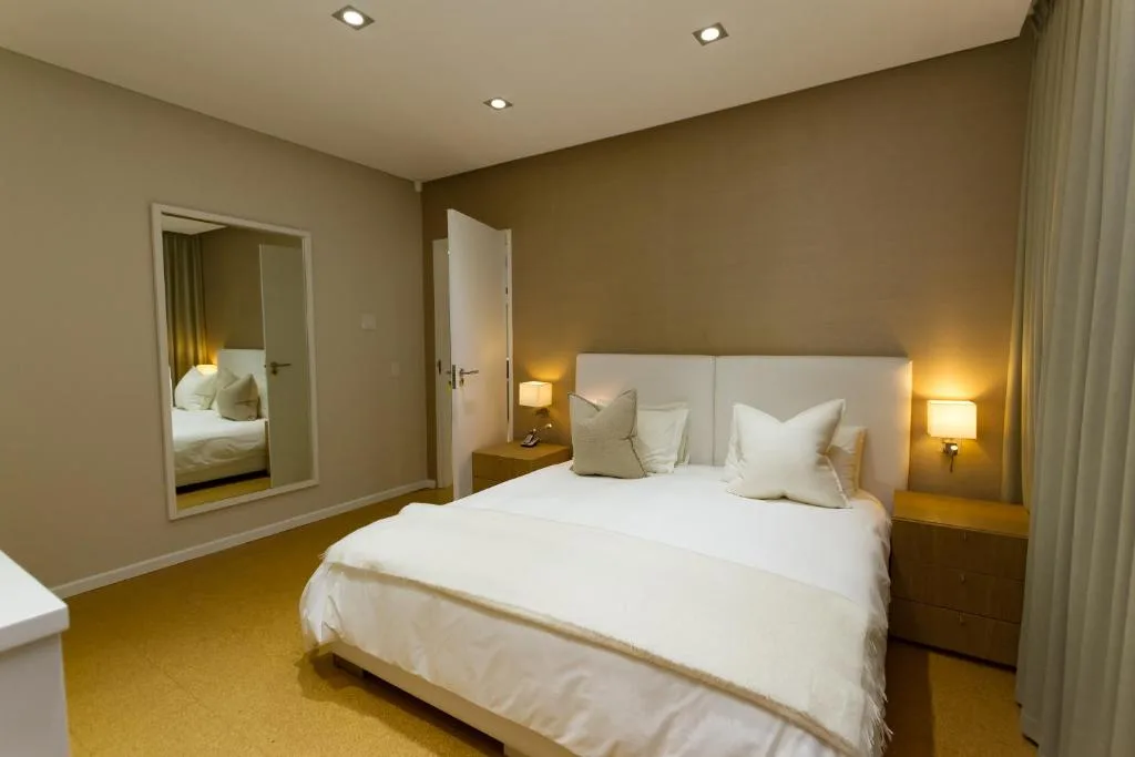Modern bedroom with white bedding, side lamps, and mirrored wardrobe