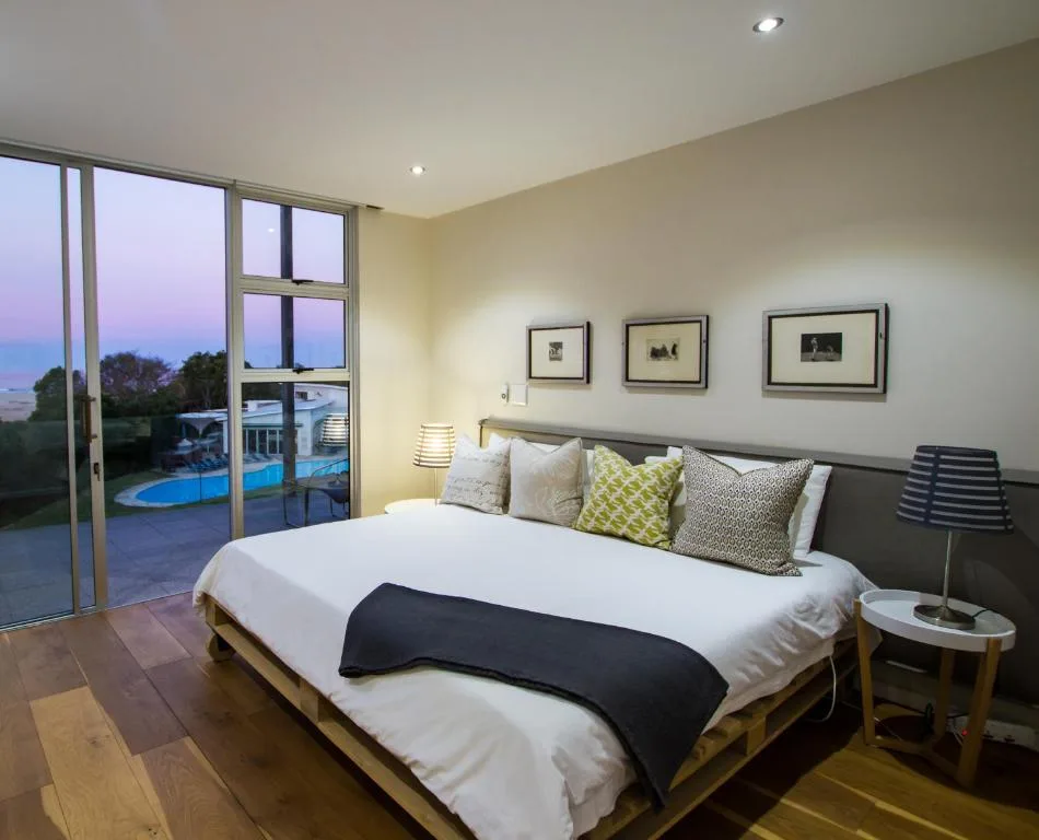 Bright bedroom with queen bed, pool view through glass doors at dusk
