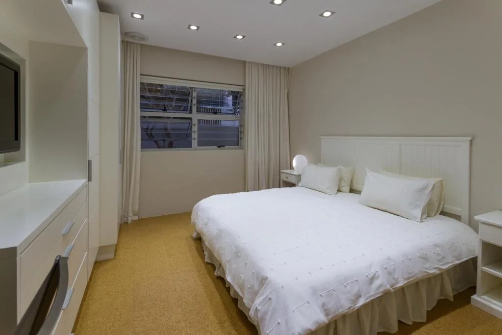 Modern bedroom with queen bed, white headboard, and large windows overlooking town