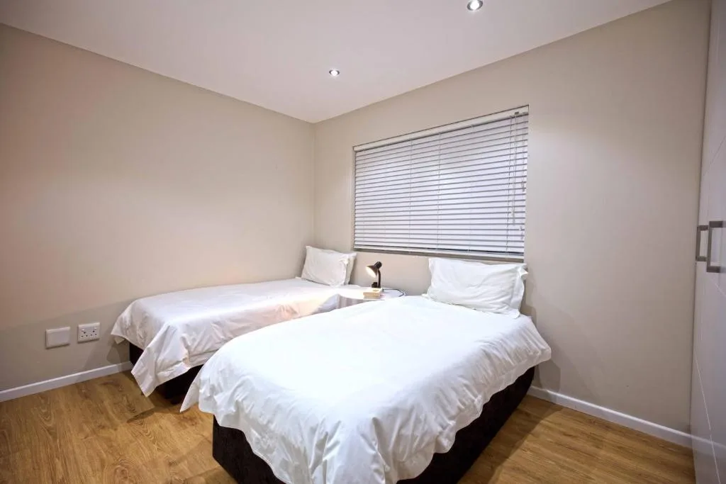Twin beds with white linens and window blinds in bright bedroom