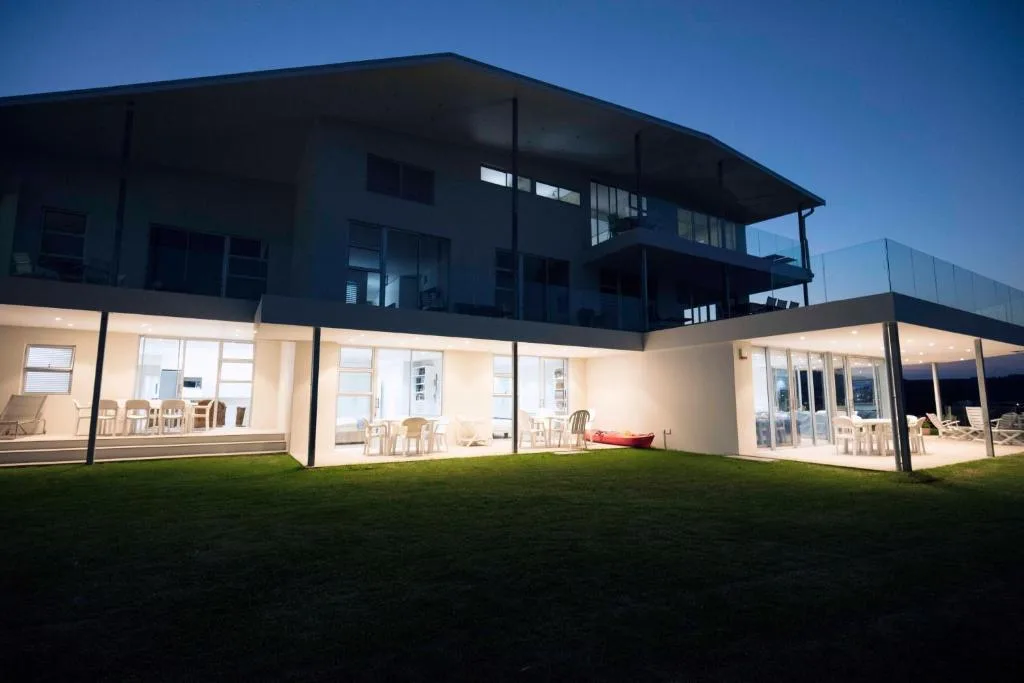 Modern two-story house with illuminated interior, manicured lawn at dusk