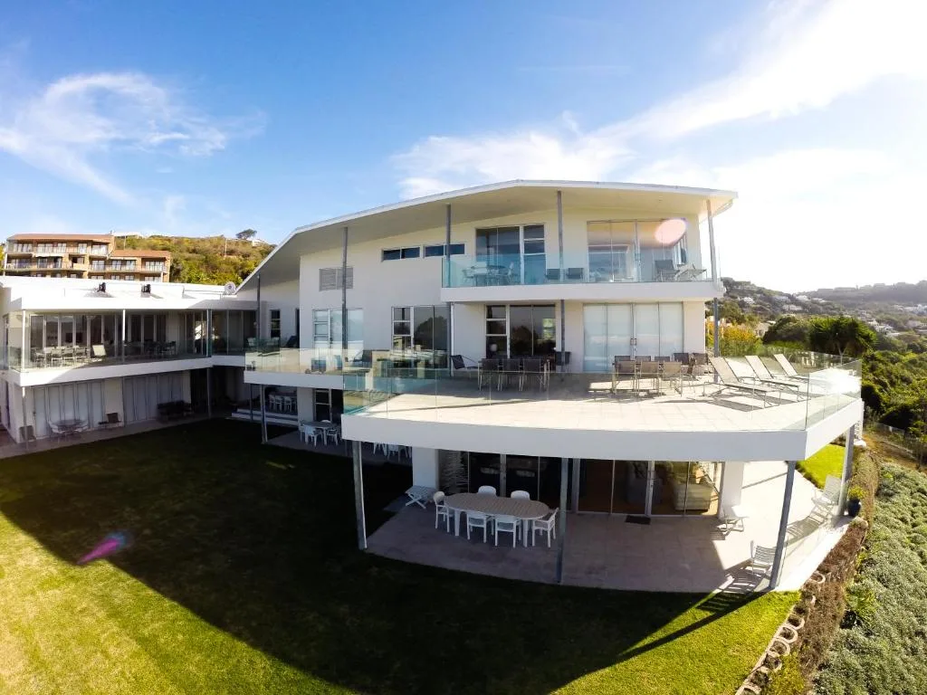 Modern white curved home with tiered decks overlooking manicured garden grounds