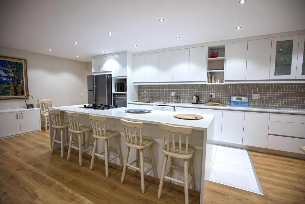 Modern white kitchen with island seating, stainless appliances, and tile backsplash
