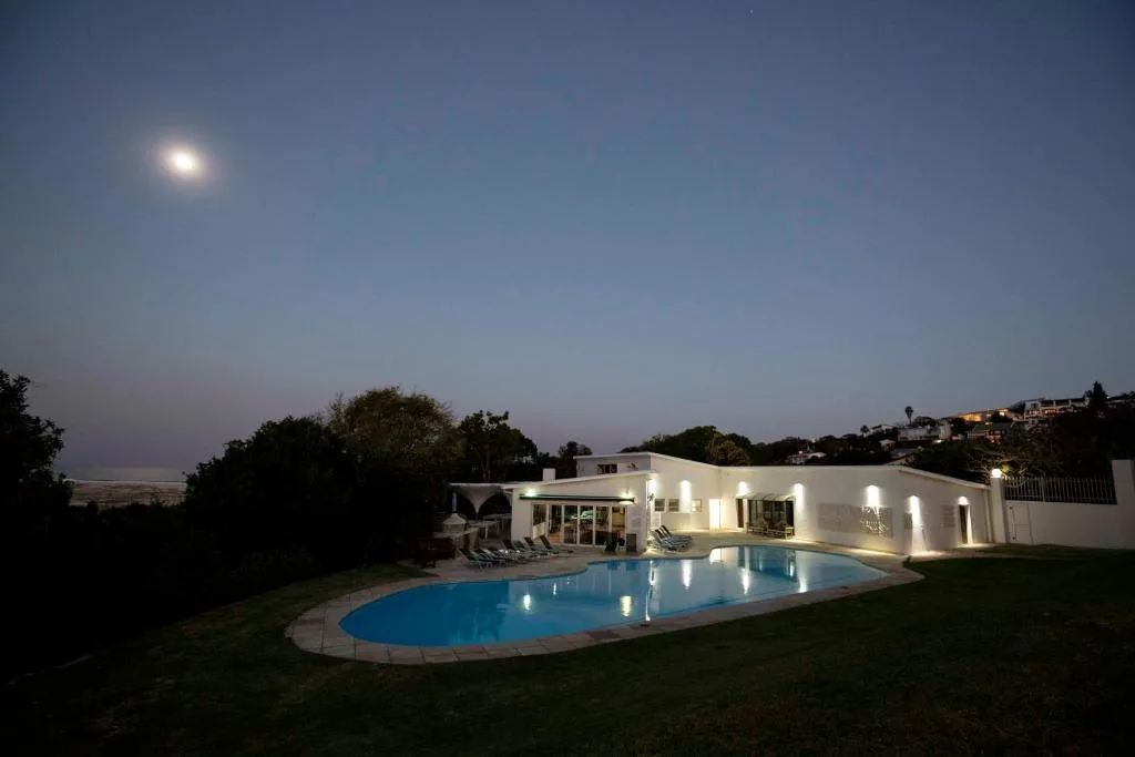 Illuminated swimming pool with modern white house and moonlit garden setting