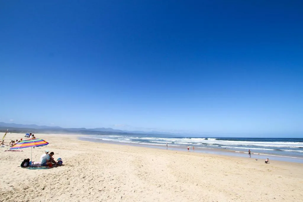Scenic beach vista with mountains and surfers in clear blue water