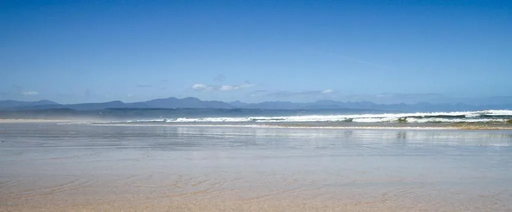 Wide sandy beach with distant mountains under clear blue sky