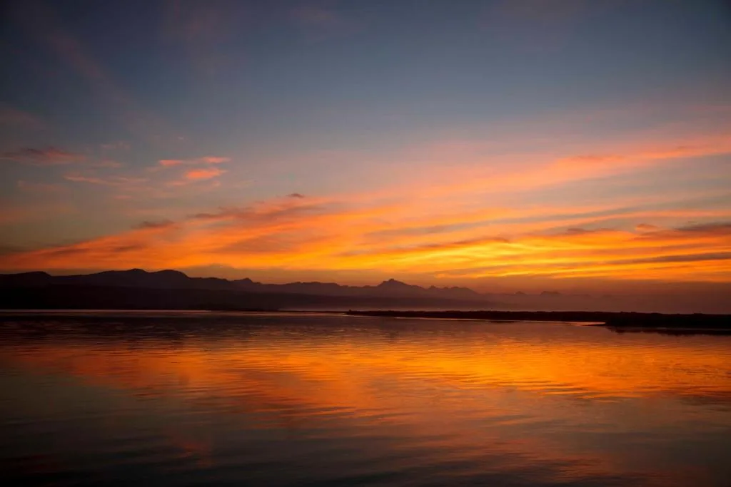 Golden sunset over calm bay waters with distant mountains silhouetted