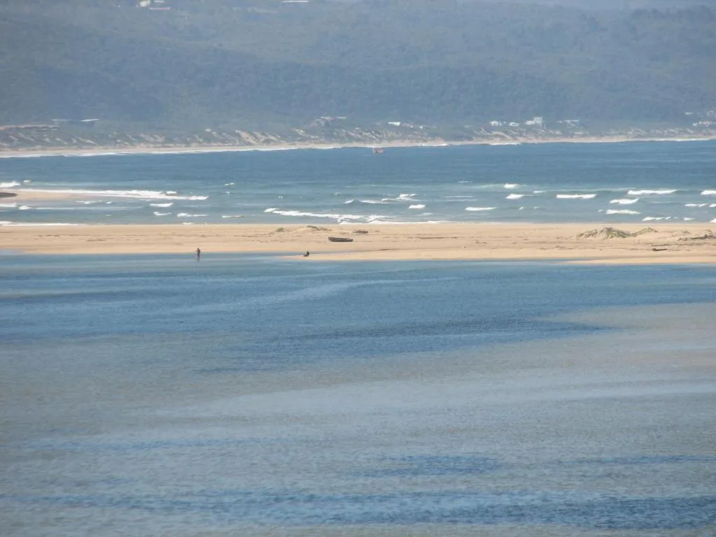 Expansive beachfront view with golden sand, rolling waves, and distant coastal mountains