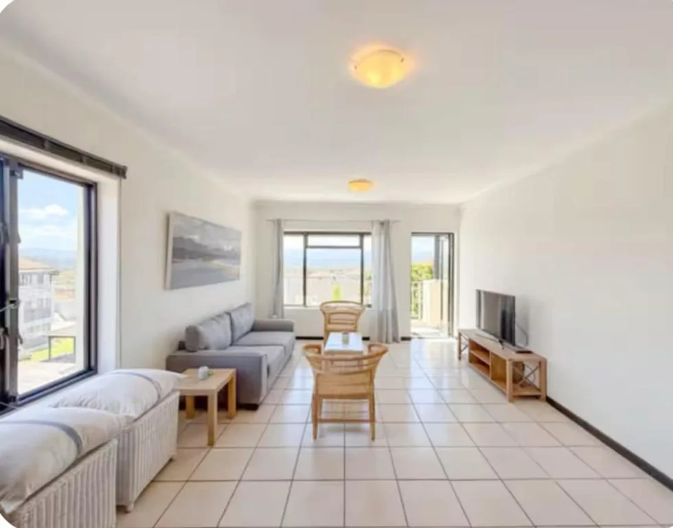 Bright open-plan lounge with sofa, wooden chairs, and panoramic windows