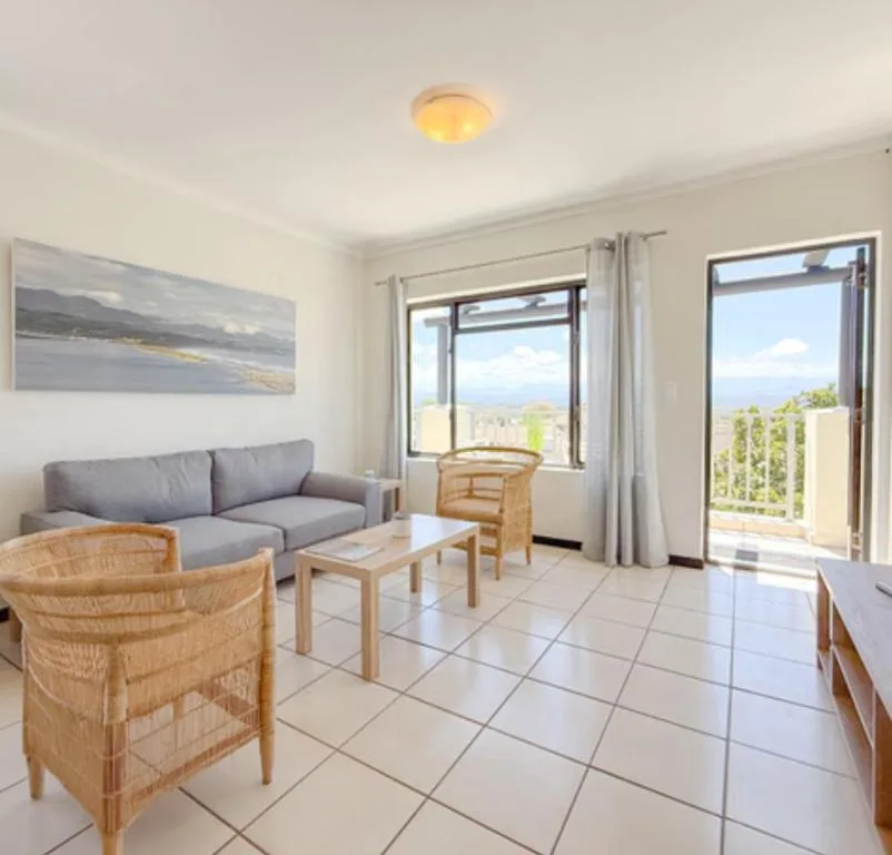 Bright lounge with gray sofa, rattan chairs, and expansive mountain views through glass doors