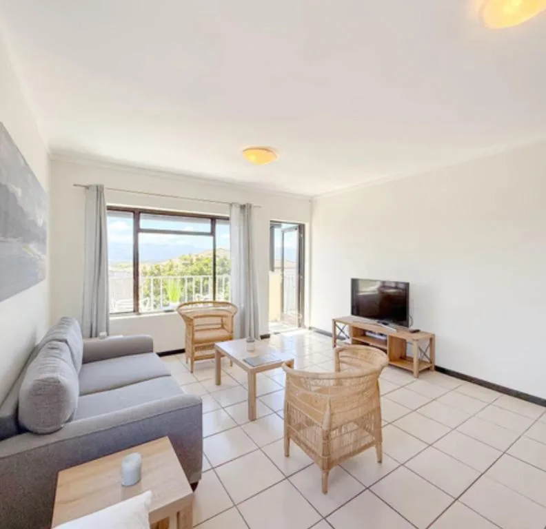 Bright living room with sofa, wicker chairs, TV, and scenic mountain views from windows