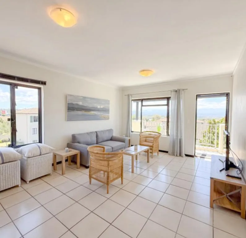 Bright lounge with gray sofa, wooden chairs, and expansive windows overlooking landscape